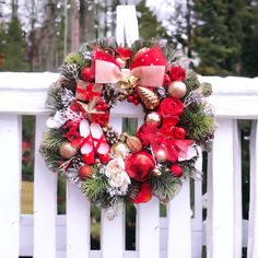 a christmas wreath on a white fence with red and gold ornaments hanging from it's sides