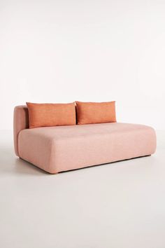 a pink couch with two orange pillows on the back and one red pillow on the side