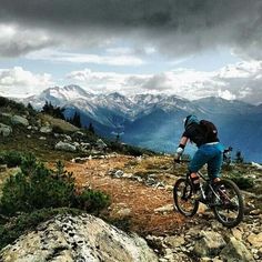 a person riding a bike on a rocky trail with mountains and clouds in the background