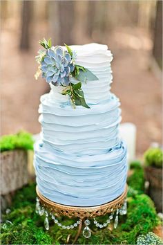 a blue tiered wedding cake with succulents and greenery on top