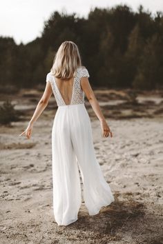 a woman standing on top of a sandy beach wearing a white dress and holding her arms out