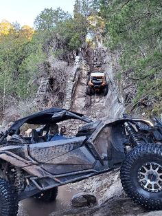 an off - road vehicle driving down a rocky trail in the woods with another vehicle behind it