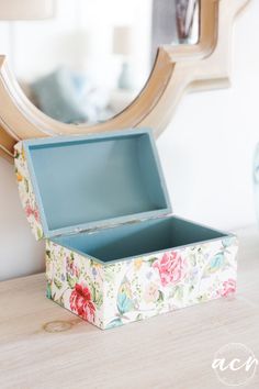 an open box sitting on top of a wooden table next to a mirror and lamp