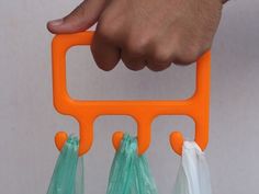 a hand holding an orange and green plastic holder with three bags attached to the handles