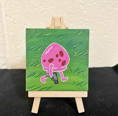 a small painting on an easel with a pink mushroom painted on the front and green background