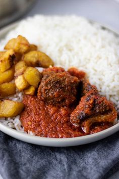 a white plate topped with rice and meat covered in sauce next to other food items