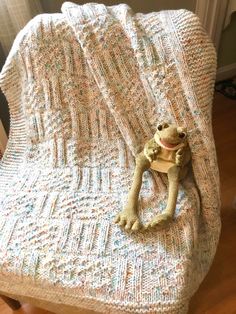 a stuffed animal sitting on top of a crocheted blanket in the shape of a frog