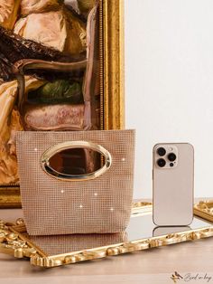 a gold purse sitting on top of a wooden table next to a cell phone and a painting