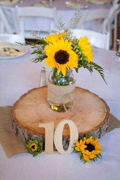 the table is set with sunflowers and greenery in vases on wood slices