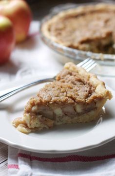 a slice of apple pie on a plate with a fork next to it and an apple in the background