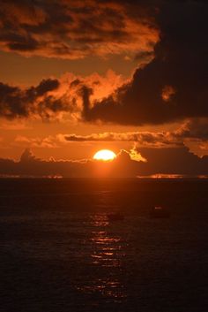 the sun is setting over the ocean with boats in the water and clouds above it