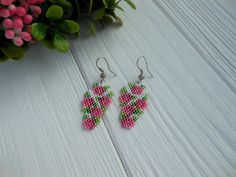 two pairs of pink and green beaded earrings on white wooden table next to potted plant