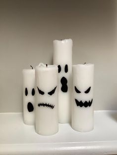 four candles with faces painted on them sitting on a shelf in front of a wall