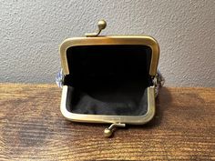 an empty gold purse sitting on top of a wooden table next to a gray wall