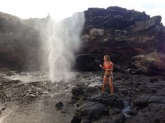 a woman standing in front of a geyser spewing water