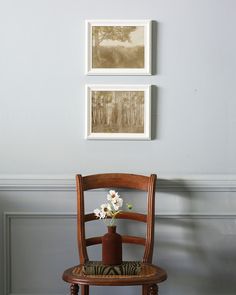 two framed pictures hang on the wall above a chair with a vase filled with flowers