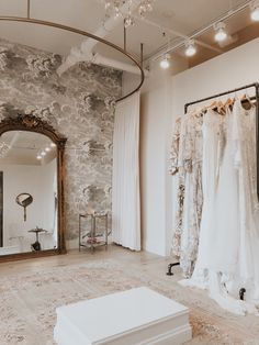 a wedding dress shop with white dresses hanging on racks and a mirror in the corner