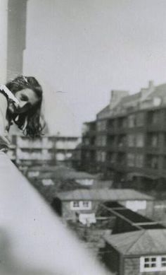 black and white photograph of a woman holding a cell phone to her ear with buildings in the background