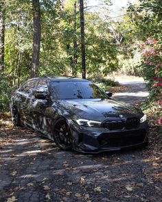 a black car parked on the side of a dirt road in front of some trees