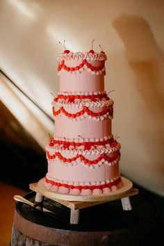 a three tiered pink cake sitting on top of a wooden barrel next to a wall