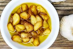 a white bowl filled with soup next to garlic and an onion on a wooden table