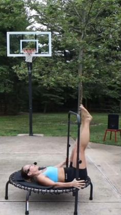 a woman laying on top of a trampoline with a basketball hoop above her head