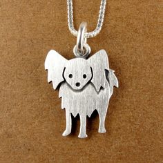 a small silver dog on a chain with its mouth open and eyes closed, sitting on a brown surface