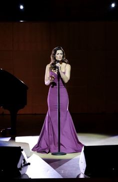 a woman in a purple dress standing next to a black piano and holding a microphone