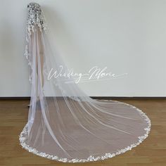 a wedding veil with white flowers on the bottom is hanging in front of a wall