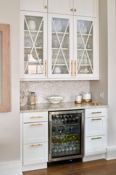 a kitchen with white cabinets and glass front wine cooler in the center, along with wood flooring