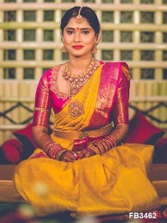 a woman sitting on top of a bed wearing a yellow and pink sari with gold jewelry