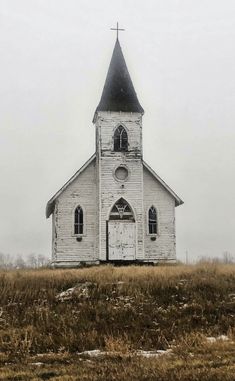 an old white church with a steeple and clock on it's side in the middle of nowhere