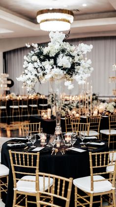 a tall vase filled with white flowers sitting on top of a black table cloth covered banquet tables