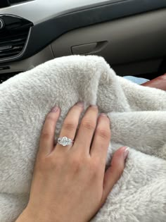 a woman's hand with a diamond ring on top of a blanket in a car