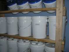 several white buckets are stacked on wooden shelves