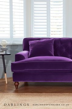 a purple couch sitting on top of a hard wood floor next to a table and window