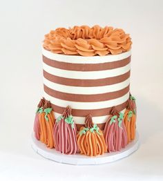 a striped cake with orange and pink frosting on it's sides, decorated with small pumpkins