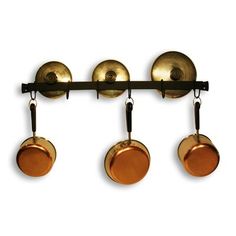 three brass pots hanging from a metal rack with four copper pans attached to it