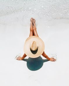 a woman in a straw hat laying on the beach