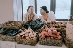 two people sitting at a table with baskets of vegetables and fruit in front of them