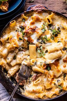 a skillet filled with pasta and cheese on top of a wooden table next to other dishes