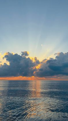 the sun shines through clouds over the ocean as it reflects in the calm water