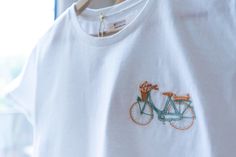 a white t - shirt with a bicycle embroidered on the front, and an orange flower in the back