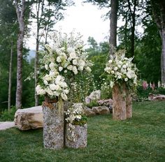 three wooden vases with flowers in them sitting on the grass next to some logs