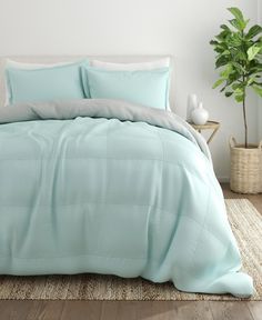 a bed with white sheets and green pillows on top of it in a room next to a potted plant