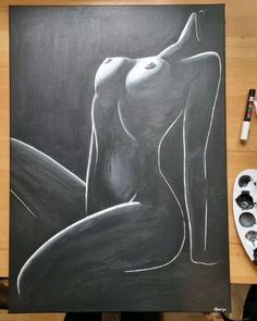 a black and white drawing of a nude woman on a wooden table next to paintbrushes