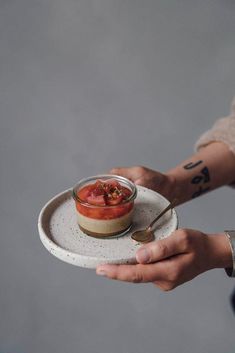 a person holding a plate with a small jar of food on it and a spoon in the other hand