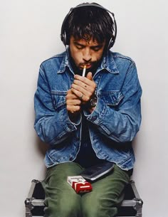 a man sitting on top of a suitcase with headphones around his ears and holding a pipe