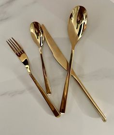 gold colored utensils and spoons sitting on a white countertop with marble background