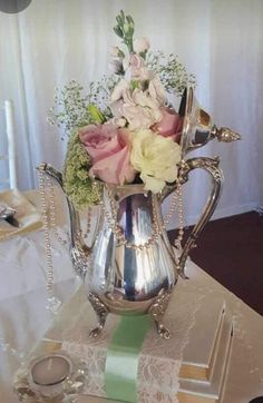 a silver vase filled with flowers sitting on top of a white tablecloth covered table